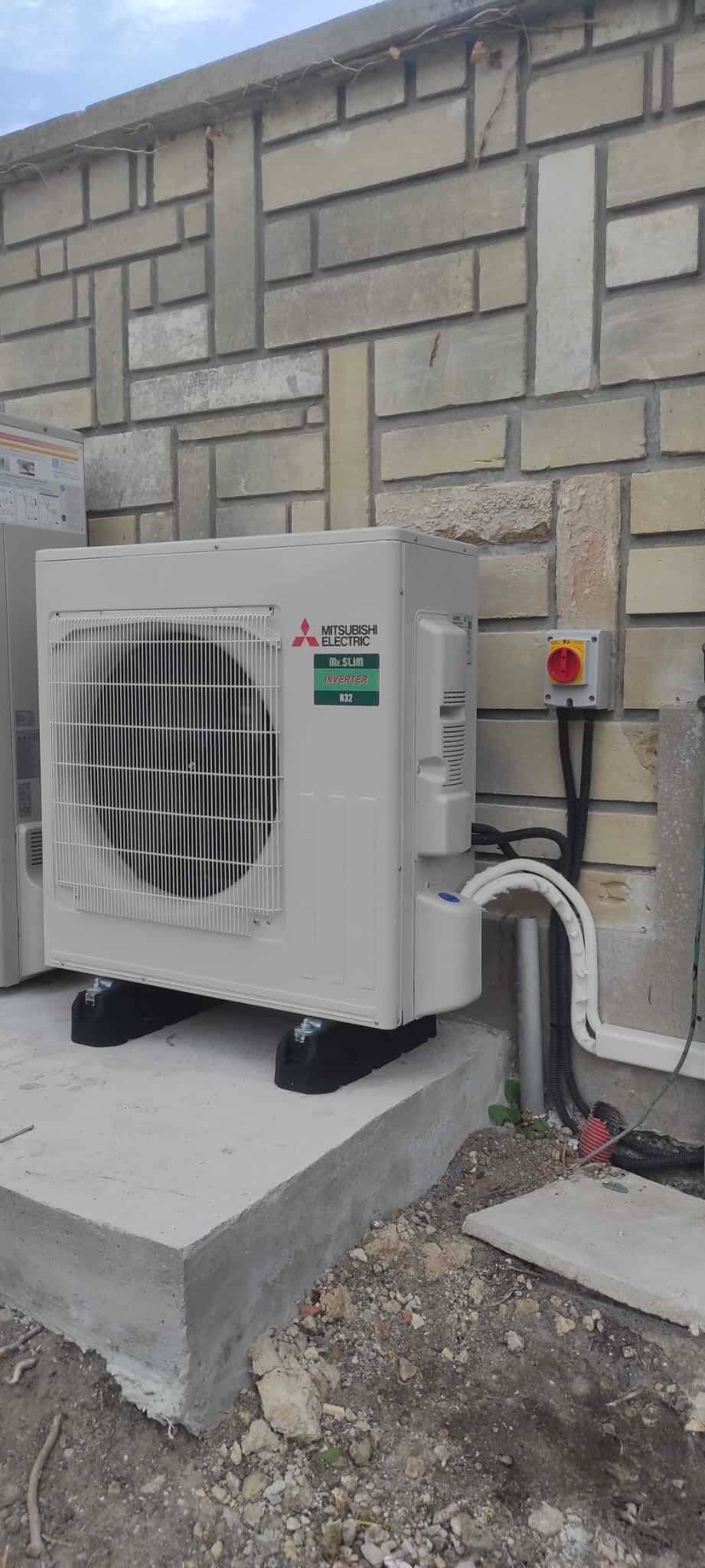 Groupe extérieur Mitsubishi Electric Mr Slim R32 installé sur plots anti-vibratiles contre un mur en pierre, avec inter-sectionneur